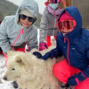 Trois enfants avec un chien de traineau lors de l'activite Cani-rando propose par la colo Neige et Soleil
