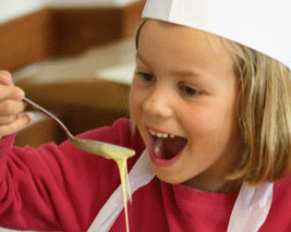 Une petite fille déguste de la pâte à crêpes lors d'un cours de cuisine avec Neige et Soleil, organisateur de colonies de vacances.